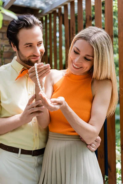 Smiling woman holding necklace near boyfriend on terrace of cafe — Stock Photo