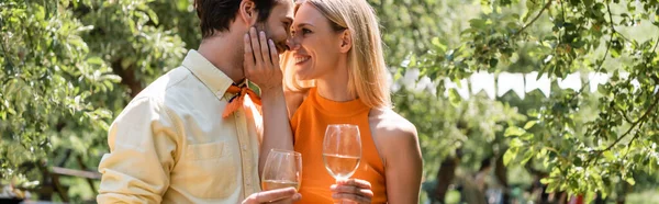 Vue latérale d'une femme joyeuse tenant un verre de vin et touchant petit ami dans un parc d'été, bannière — Photo de stock