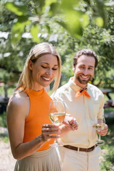 Femme gaie tenant un verre de vin près du petit ami flou dans le parc d'été — Photo de stock