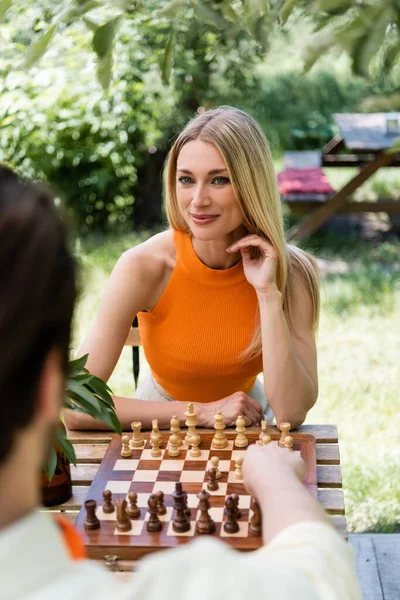 Smiling woman looking at blurred boyfriend near chessboard in park — Stock Photo