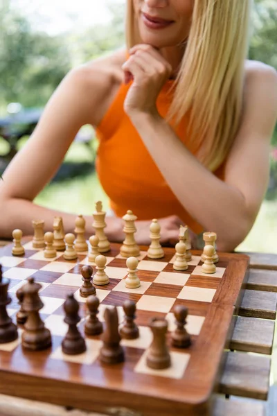 Ausgeschnittene Ansicht einer Frau, die in der Nähe eines Schachbretts im Park sitzt — Stockfoto