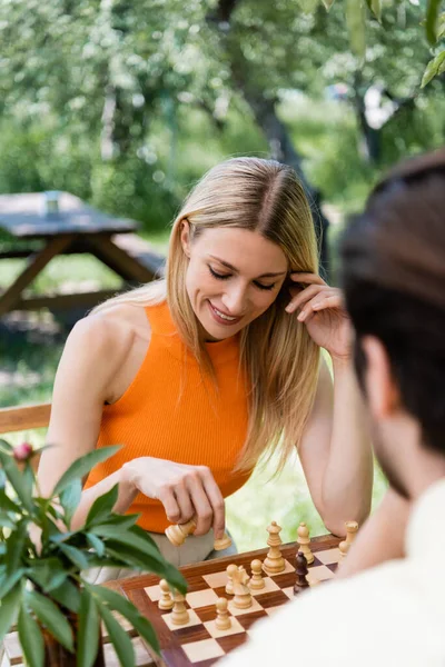 Mujer positiva jugando ajedrez con novio borroso en el parque - foto de stock