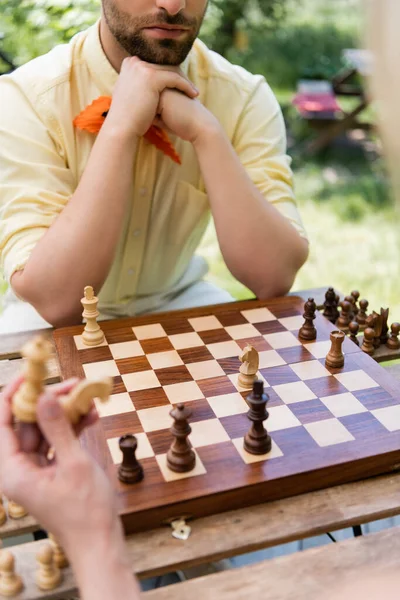Cropped view of man sitting near blurred girlfriend holding chess in park — Stock Photo