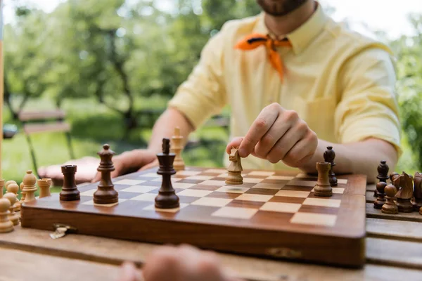Обрізаний вид розмитого чоловіка, який грає в шахи в літньому парку — стокове фото