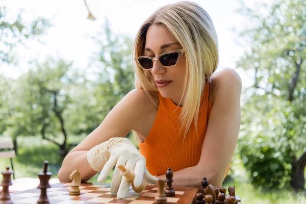 Trendy woman in sunglasses playing chess in park — Stock Photo