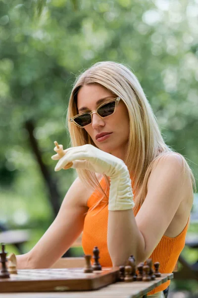 Модна жінка тримає шахову фігуру біля дошки в парку — стокове фото