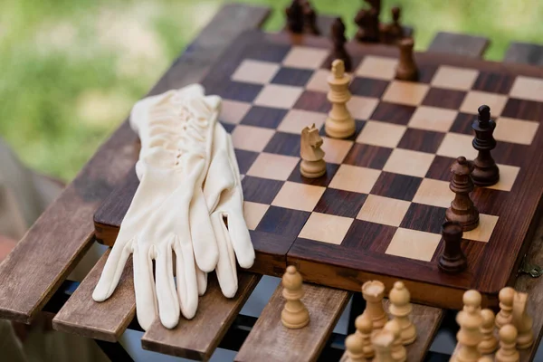 Guantes cerca de figuras de madera en tablero de ajedrez en el parque - foto de stock