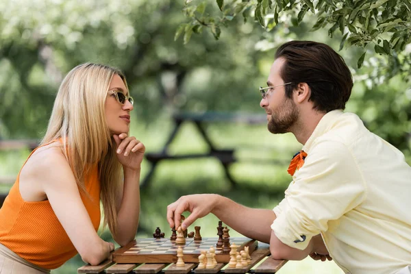 Pareja con estilo en gafas de sol jugando ajedrez en el parque - foto de stock