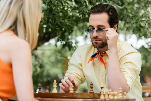 Joven sosteniendo gafas de sol cerca del ajedrez y novia borrosa en el parque — Stock Photo