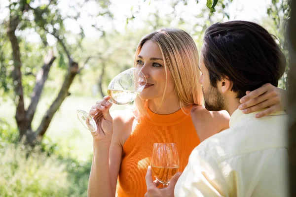 Smiling woman drinking wine and hugging boyfriend in summer park — Stock Photo
