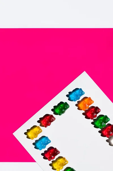 Colocación plana de osos gomosos de colores sobre fondo blanco y rosa - foto de stock