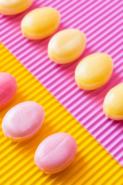 Flache Lage mit süßen Bonbons auf texturiertem rosa und gelben Hintergrund — Stockfoto