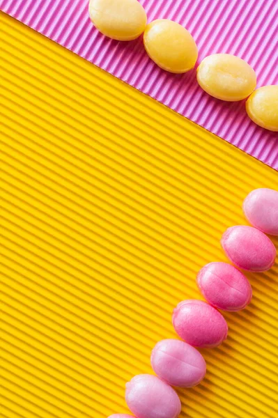 Flache Lage von bunten Bonbons auf texturiertem rosa und gelben Hintergrund — Stockfoto