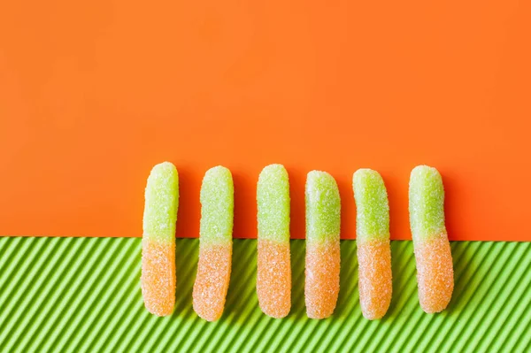 Vista superior de dulces de gelatina en la superficie naranja y verde - foto de stock