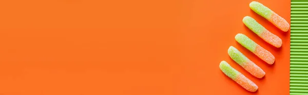Draufsicht auf bunte Gummibonbons auf grüner und orangefarbener Oberfläche, Banner — Stockfoto