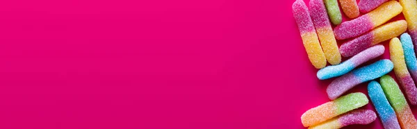 Acostado plano con dulces de goma de colores con azúcar en la superficie de color rosa, pancarta - foto de stock
