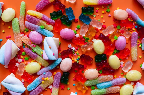 Vista dall'alto di caramelle colorate gelatina e marshmallow su sfondo arancione — Foto stock