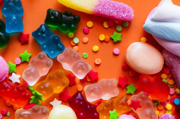 Vista dall'alto di colorati orsi gelatina vicino caramelle e decorazioni su sfondo arancione — Foto stock