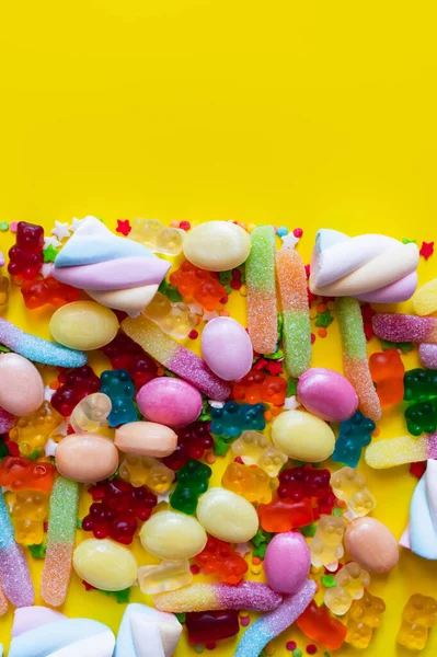 Vue de dessus des guimauves moelleuses et des bonbons à la gelée sur la surface jaune — Photo de stock