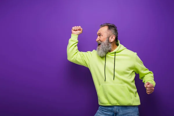 Glücklicher und bärtiger älterer Mann mit grauen Haaren jubelt, während er lila wegsieht — Stockfoto