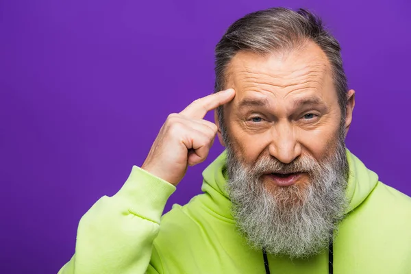 Nachdenklicher älterer Mann zeigt auf Tempel und blickt in Kamera auf lila — Stockfoto