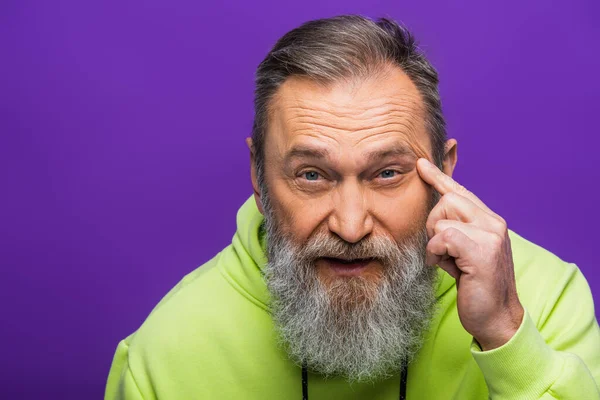 Homem sênior com barba tocando rosto com rugas e olhando para a câmera isolada em roxo — Fotografia de Stock