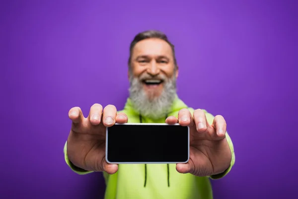 Heureux homme âgé avec barbe et cheveux gris tenant smartphone avec écran vierge sur violet — Photo de stock