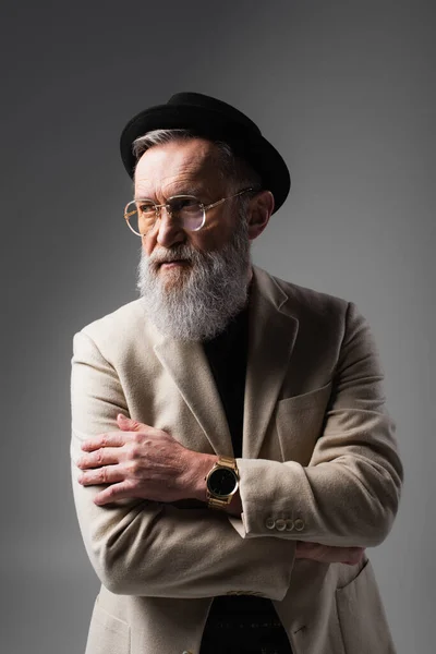 Stylish senior man in beige jacket and derby hat posing on grey — Stock Photo