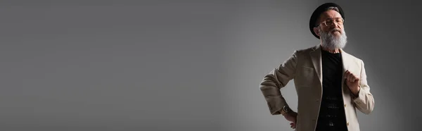 Stylischer Senior in beiger Jacke und Derbyhut posiert mit Hand auf Hüfte auf grau, Banner — Stockfoto
