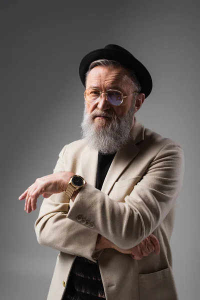 Stylish senior man in beige jacket and derby hat looking at camera on grey — Stock Photo