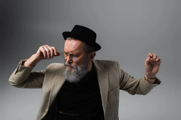 Bearded senior man in derby hat and eyeglasses gesturing on grey — Stock Photo