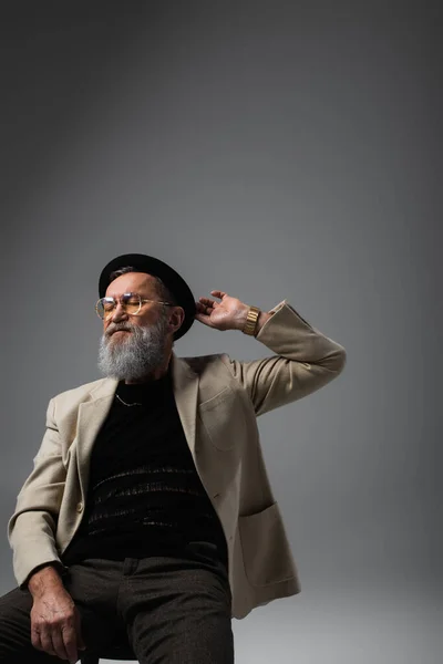 Homme âgé barbu en lunettes et veste réglage derby chapeau sur gris — Photo de stock