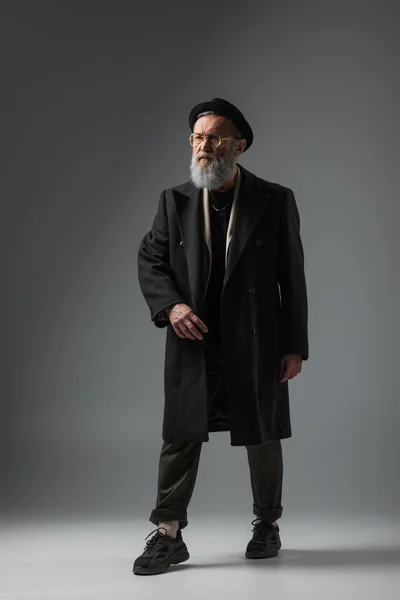 Full length of elegant senior man in autumnal coat and derby hat posing on grey — Stock Photo