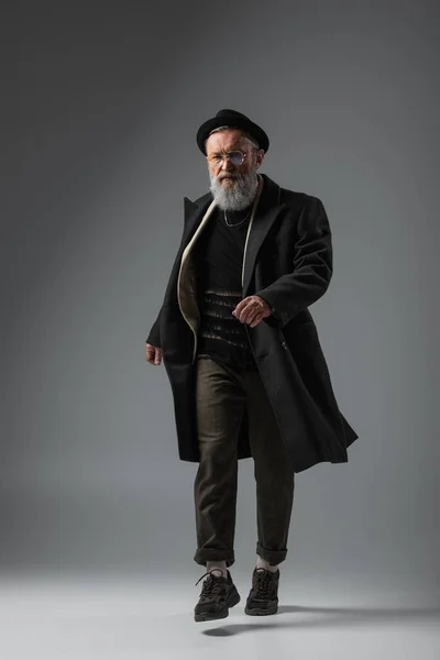 Full length of elegant senior man in coat and derby hat walking on grey — Stock Photo