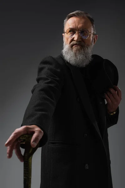Eleganter älterer Herr im schicken Mantel mit Derbyhut und Gehstock auf grau — Stockfoto