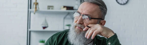 Nachdenklicher und bärtiger älterer Herr mit Brille, Stift in der Hand und daheim wegschauend, Banner — Stockfoto