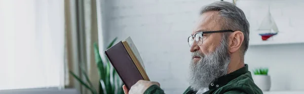 Homme âgé barbu dans des lunettes de lecture livre à la maison, bannière — Photo de stock