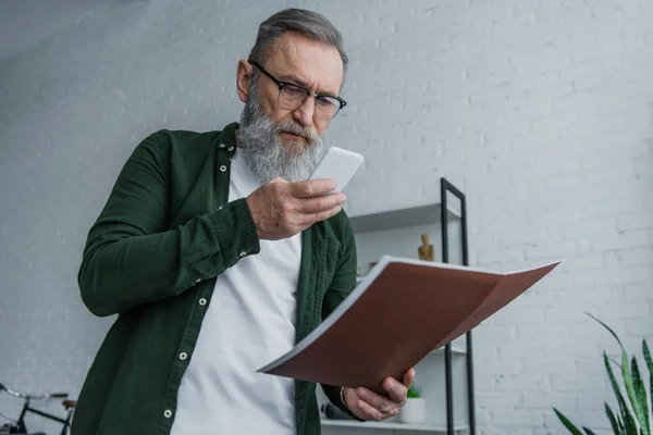 Hombre mayor barbudo en gafas de vista tomar foto de la carpeta en el teléfono inteligente - foto de stock