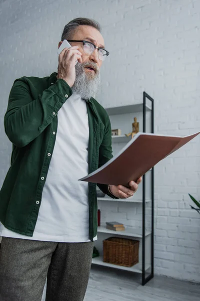 Senior-Geschäftsmann mit Bart in Brille steht mit Ordner beim Telefonieren auf dem Smartphone — Stockfoto