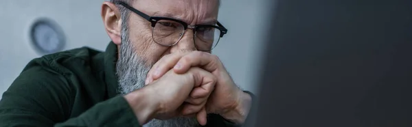 Homme âgé stressé dans les lunettes fronçant les sourcils et couvrant le visage avec les mains serrées, bannière — Photo de stock