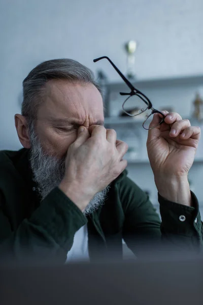 Tired senior man with beard touching closed eyes and holding eyeglasses — Stock Photo
