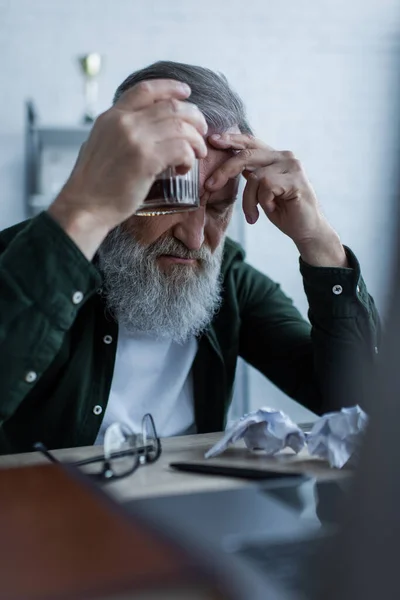 Chateado homem sênior com barba segurando copo de uísque enquanto sofre crise — Fotografia de Stock