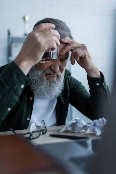 Molesto hombre mayor con barba sosteniendo un vaso de whisky mientras sufre una crisis - foto de stock