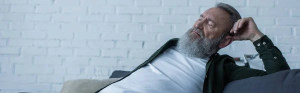 Bouleversé homme âgé avec la barbe souffrant crise alors qu'il était assis sur le canapé dans le salon, bannière — Photo de stock