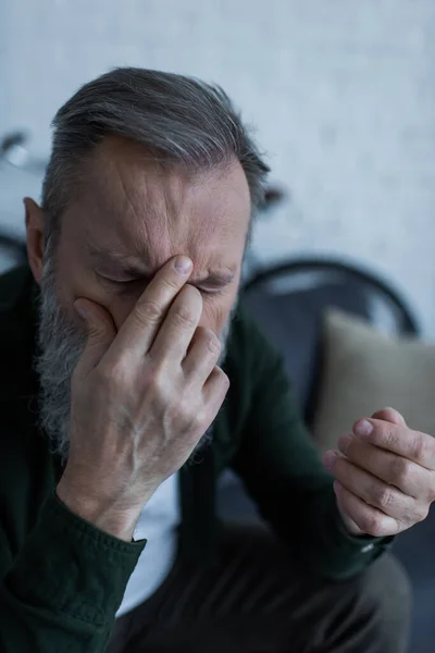 Senior Mann mit Bart bedeckt Gesicht, während er unter Kopfschmerzen leidet — Stockfoto