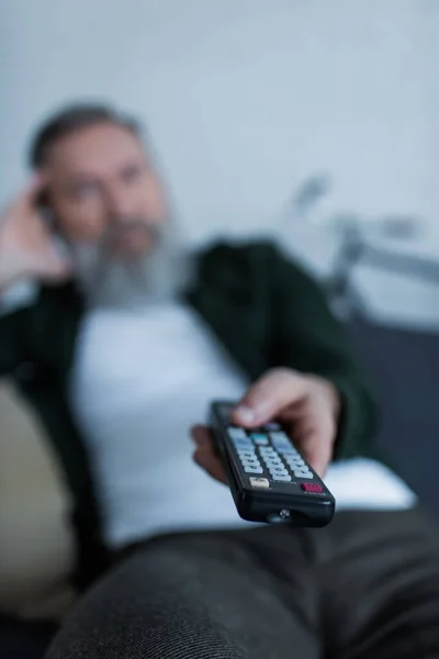 Flou homme âgé tenant télécommande tout en regardant la télévision — Photo de stock
