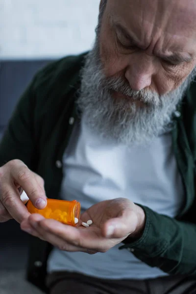 Malheureux homme âgé avec des cheveux gris tenant bouteille avec des pilules anti-dépresseurs — Photo de stock