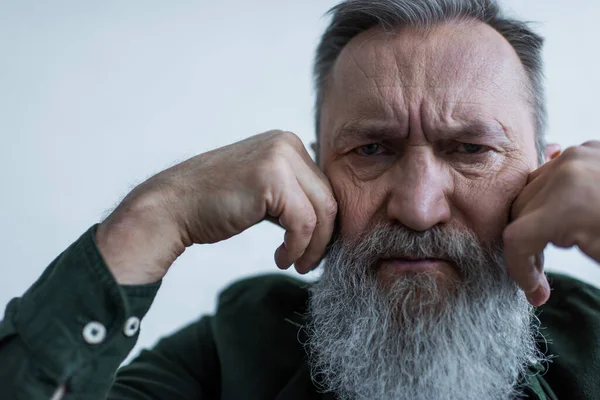 Portrait of displeased senior man with beard frowning while looking at camera — Stock Photo