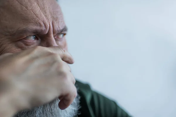 Portrait of displeased senior man with beard frowning while looking away and covering face with hand — Stock Photo
