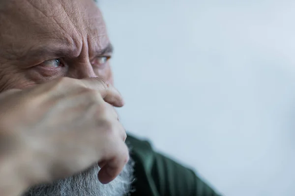 Portrait de l'homme âgé mécontent avec barbe fronçant les sourcils tout en regardant loin et couvrant le visage avec la main — Photo de stock